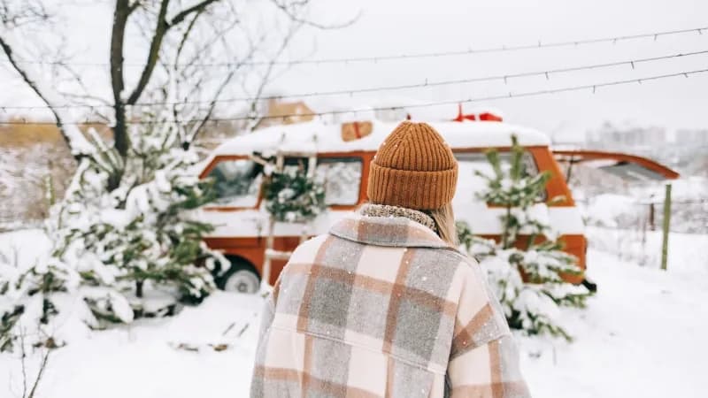 Junge Frau steht im Schnee vor ihrem Minicamper