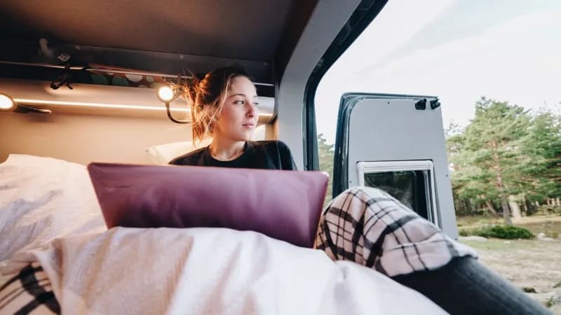 Junge Frau sitzt mit ihrem Laptop im Minicamper