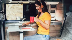 Frau mit gelbem T-Shirt sitzt im Minicamper am Laptop
