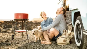 Ein Paar sitzt mit Hund und Grill von dem Minicamper