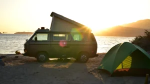 Minicamper steht am Strand bei Sonnenuntergang